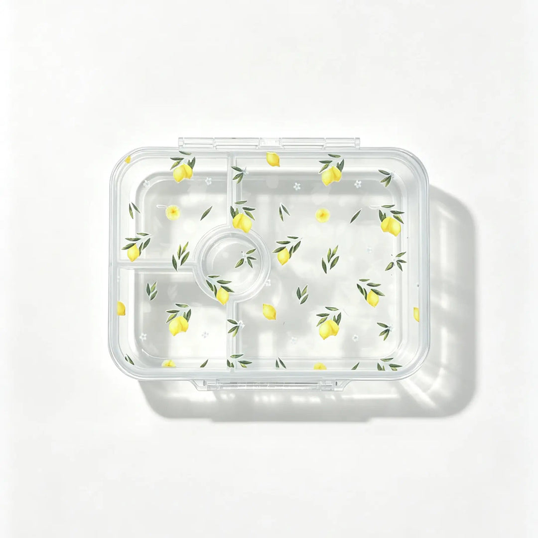 A clear plastic bento container with multiple compartments, decorated with a repeating pattern of yellow lemons and green leaves, shown from a top-down view on a white background.