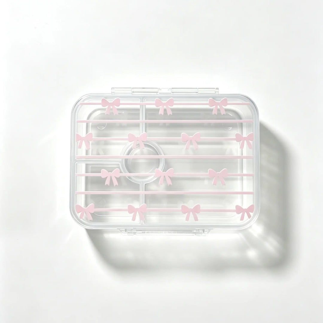 A clear plastic bento with a lid decorated with small pink bow patterns, shown on a clean white background with a soft shadow.