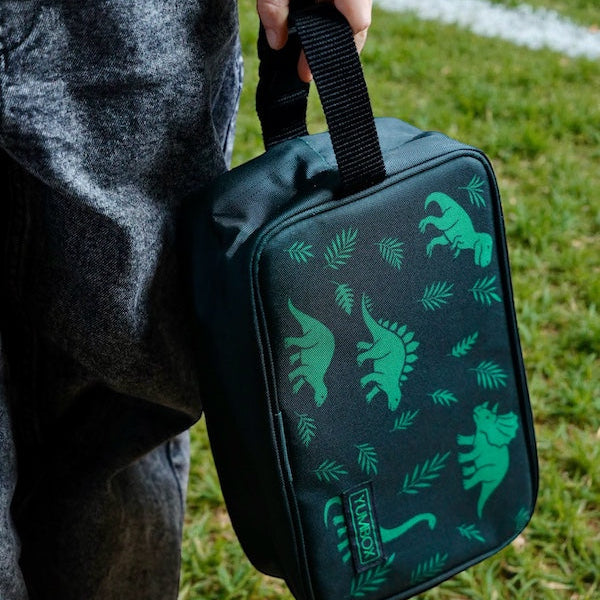 Person holding a dark green bag with dinosaur patterns on grass