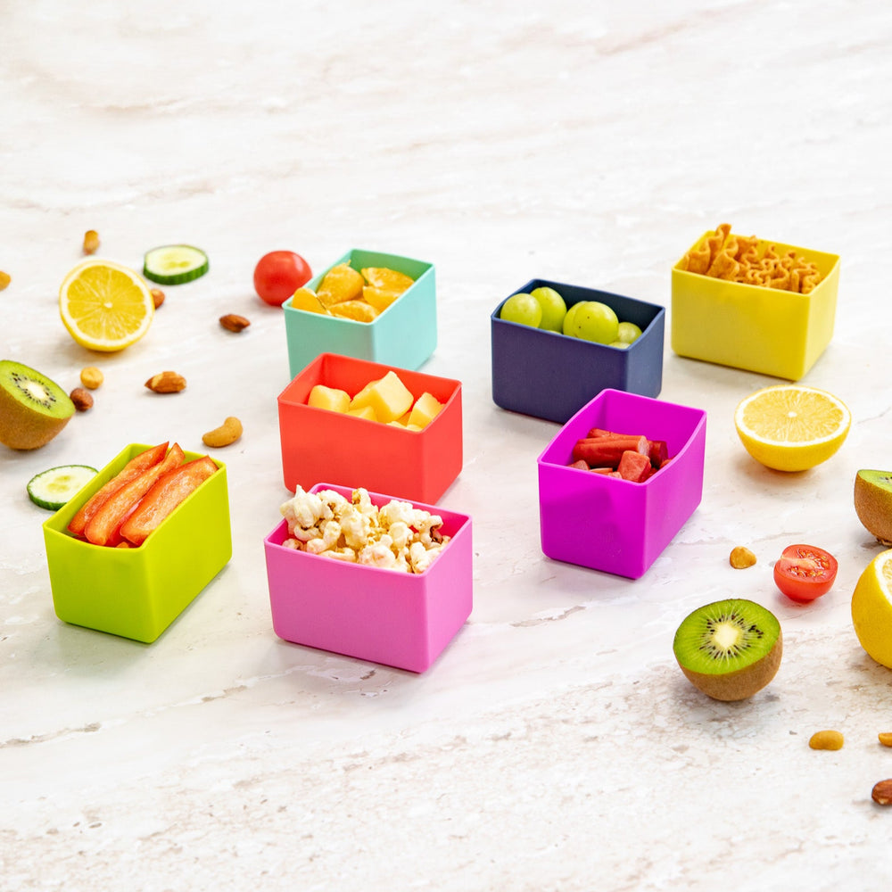 Colorful silicone snack containers with fruits and snacks on a light surface