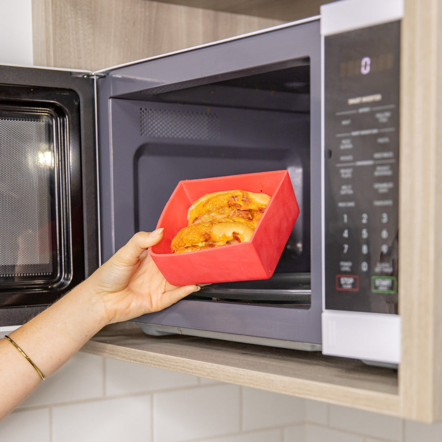 Person using a red silicone baking dish to cook food in a microwave.