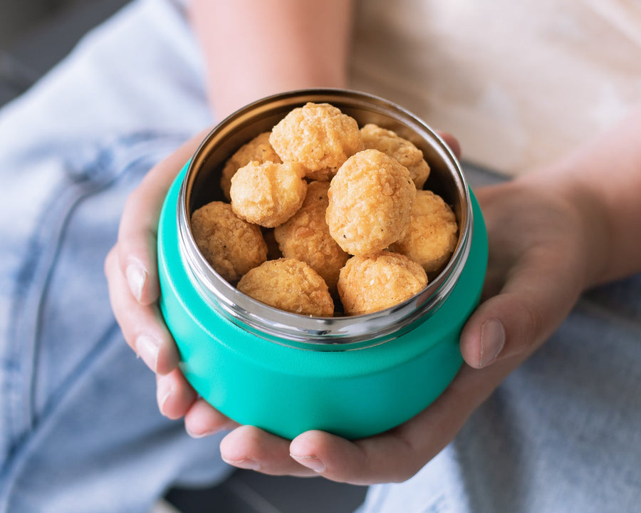 A person holding a green insulated food jar filled with snacks.
