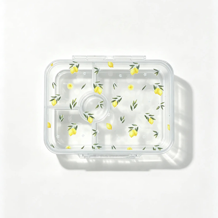 A clear plastic bento container with multiple compartments, decorated with a repeating pattern of yellow lemons and green leaves, shown from a top-down view on a white background.